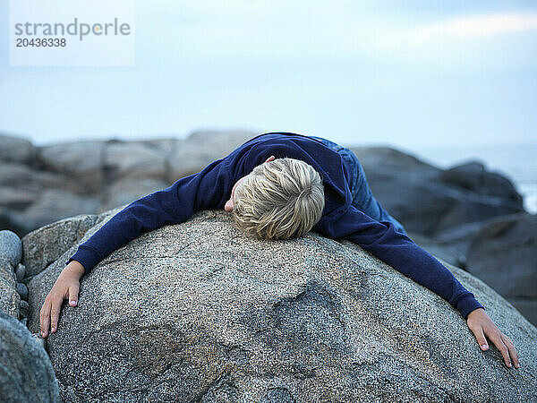 boy drapes over rock on rocky maine coast