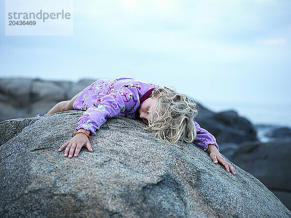 girl drapes herself over a rock on maine's rocky coast