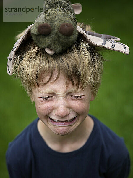 Young boy cries  with stuffed animal on his head.