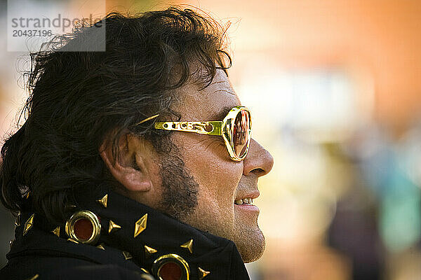 Elvis impersonator in a black costume with gold sunglasses on.