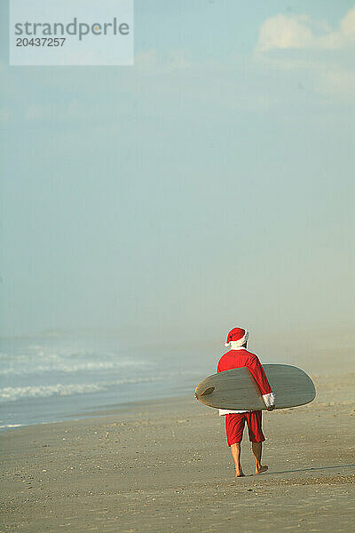 A man Dressed as Santa at the Beach with a surfboard