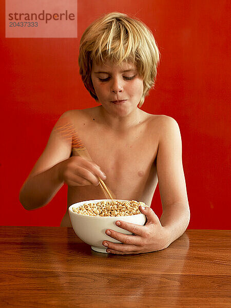 A boy eats cereal with chopsticks.