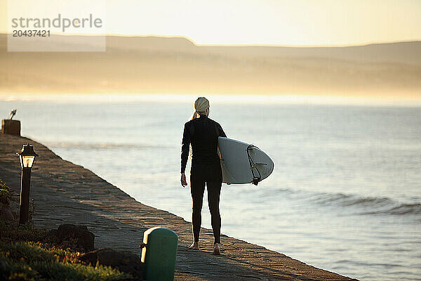 A woman surfer walks on a path near the ocean in Baja Mexico.