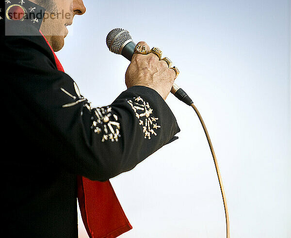 Elvis impersonator holding a microphone on stage performing in front of a crowd.