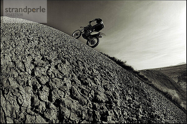 Dust and dirt fly as a young man climbs a steep hill on his dirt bike into a hard turn while motocross riding on the surreal dunes near Cameron  AZ.