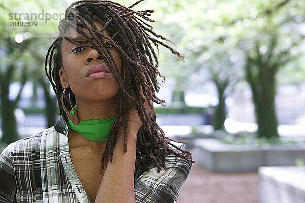 Portrait of a young woman with hair in dreads  in a city park.