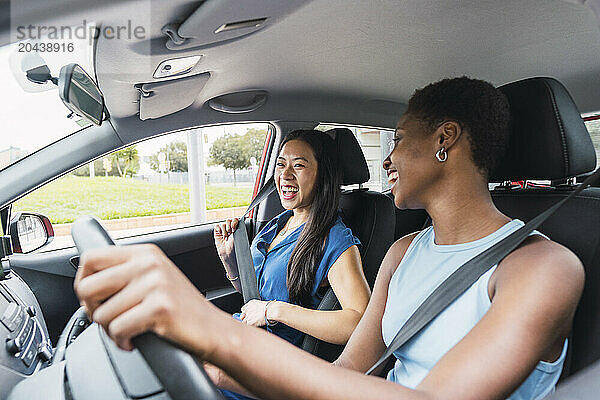 Cheerful young woman driving car sitting with friend