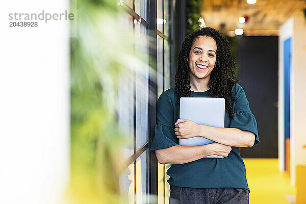 Happy businesswoman holding laptop standing at coworking space