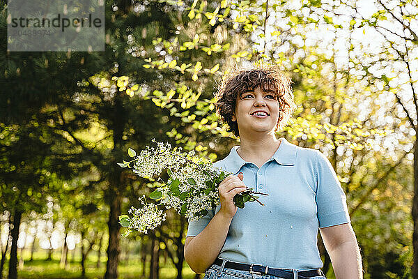 Smiling young woman holding bunch of flowers at park