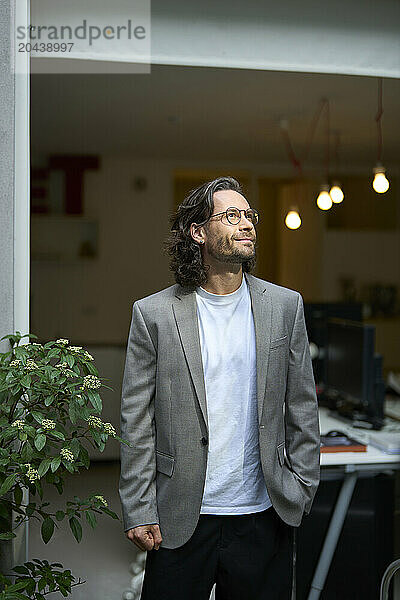 Thoughtful mature businessman standing with hand in pocket at office