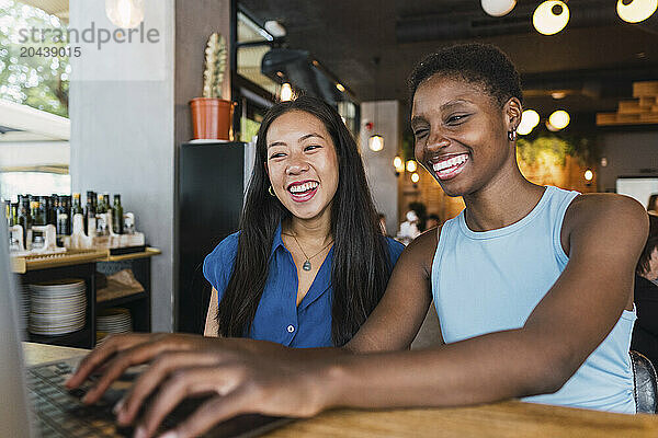 Happy friends sharing laptop sitting in cafe