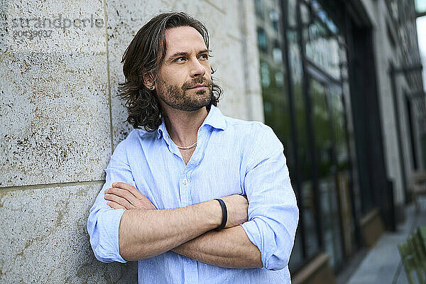 Handsome mature man with arms crossed leaning on wall