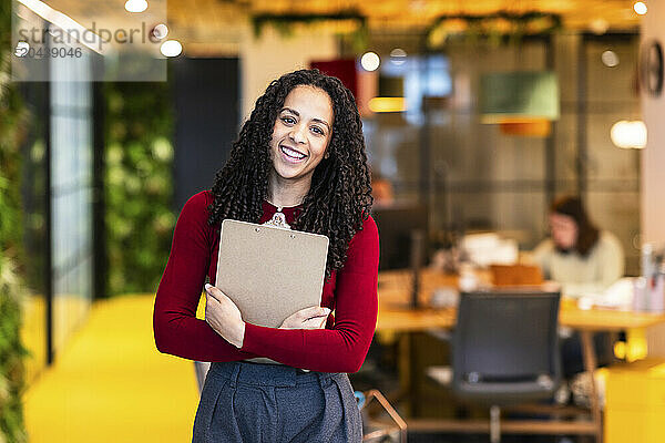 Smiling businesswoman holding clipboard standing at office