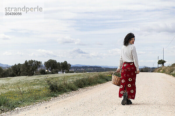 Smiling young woman walking with wicker basket on road