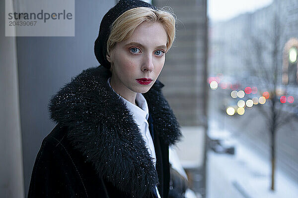 Beautiful blond woman wearing fur coat and standing in balcony