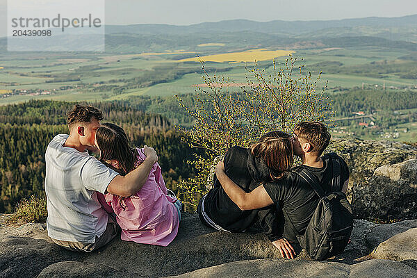 Young couples kissing each other and sitting on rock