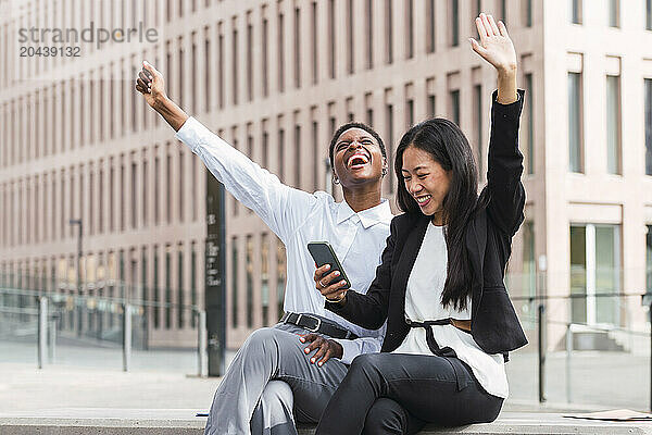 Cheerful business colleagues sharing smart phone sitting at office park