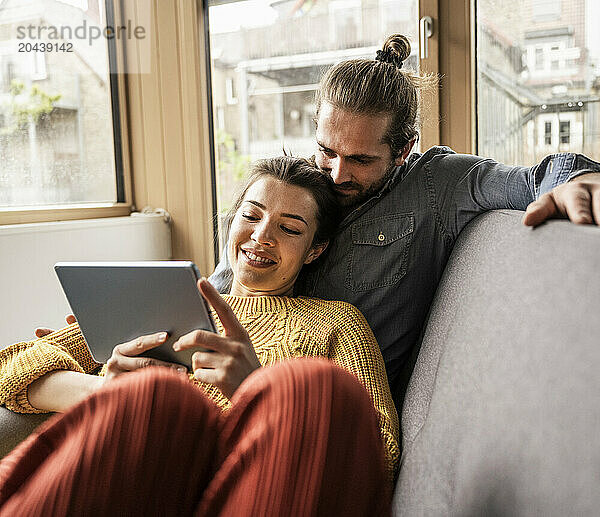 Young boyfriend and girlfriend watching tablet PC on sofa at home