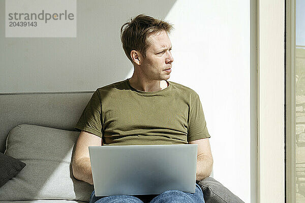 Mature man with laptop looking out of window