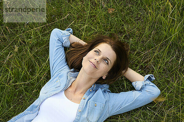 Thoughtful woman with hands behind head lying on grass