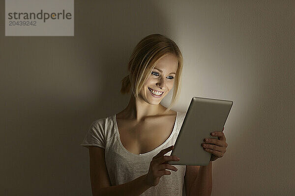 Smiling blond woman using tablet PC in front of wall