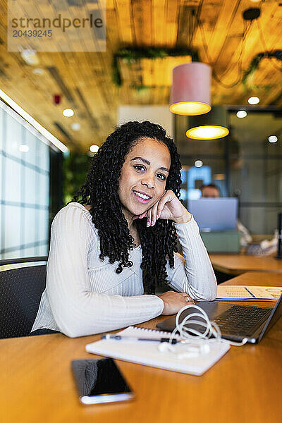 Businesswoman with curly hair leaning on elbow at desk in office