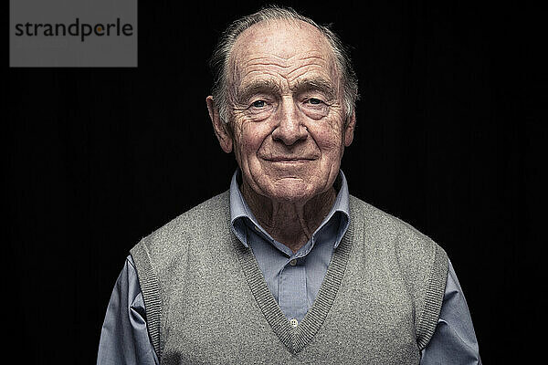 Retired man smiling against black background