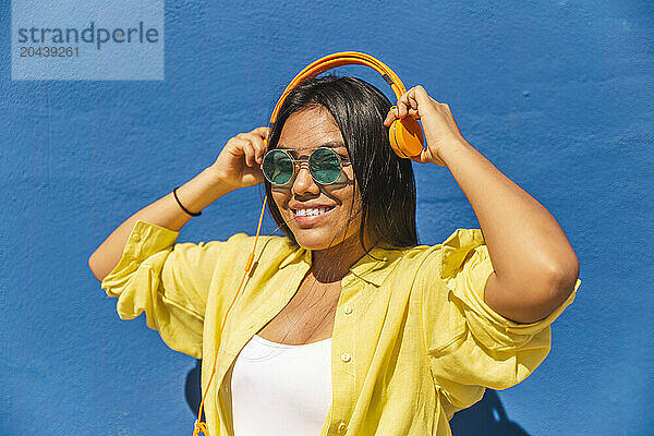 Smiling woman with headphones in front of wall