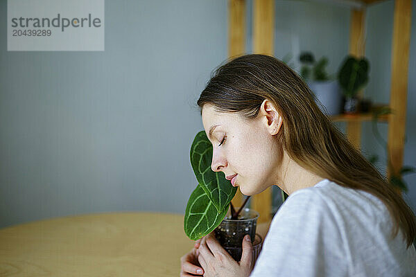 Woman with eyes closed hugging potted plant at home