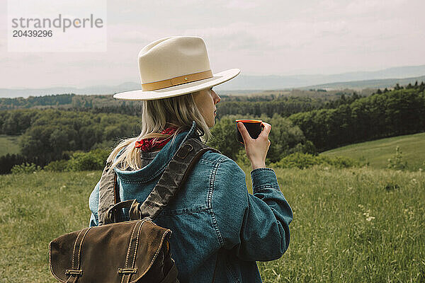 Stylish woman holding backpack and drinking warm tea