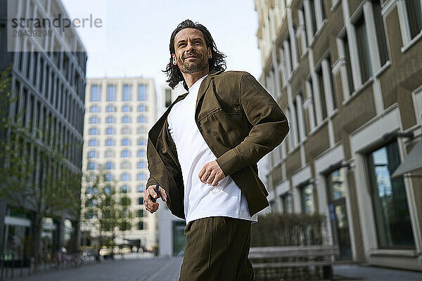 Smiling mature man running in front of modern buildings