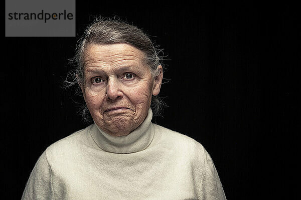 Senior woman with facial expression standing against black background