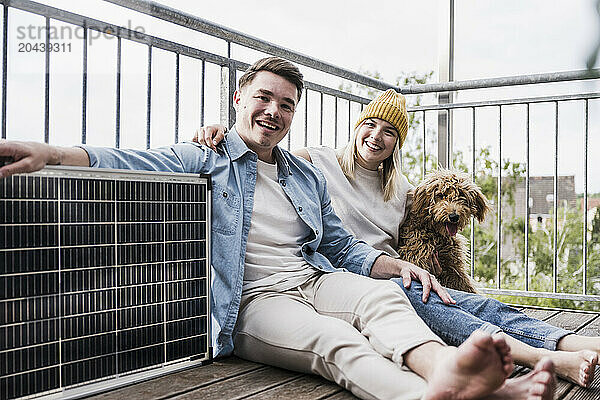 Happy young couple sitting with solar panel and dog