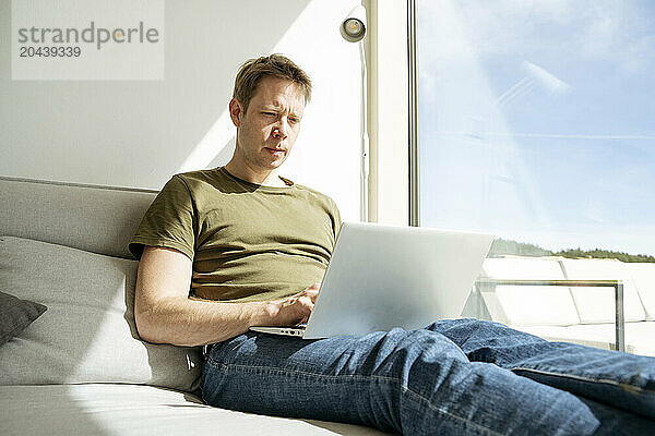 Mature freelancer working on laptop by window at home