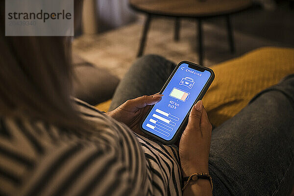 Young woman operating electric car charging mobile app at home