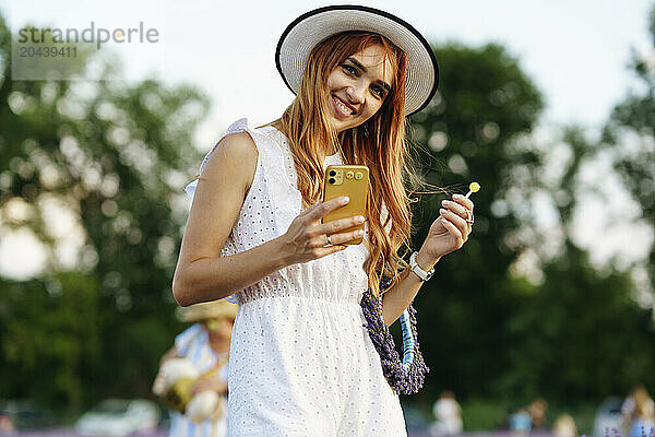 Happy woman standing with smart phone at field