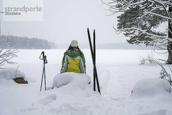 Woman taking break and sitting on rock in winter forest