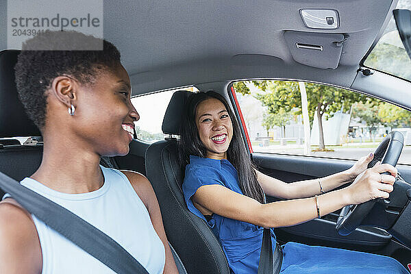 Happy young woman sitting with friend driving car