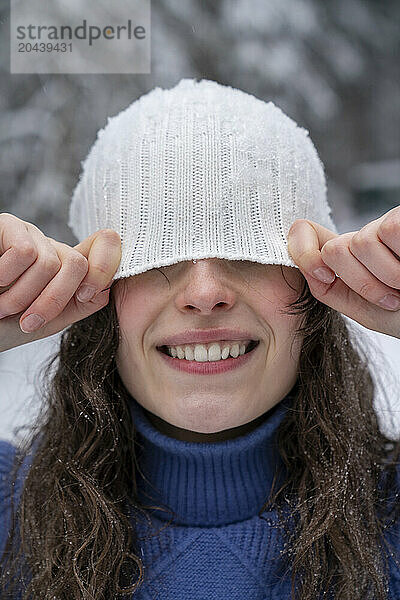 Young woman hiding face with knit hat in winter forest