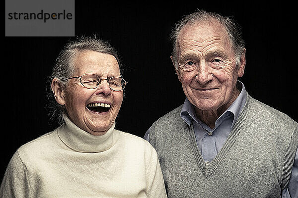 Senior couple smiling and laughing against black background