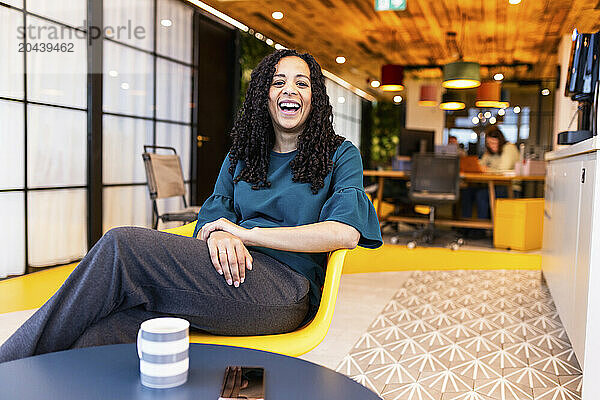 Happy businesswoman sitting on chair at coworking space