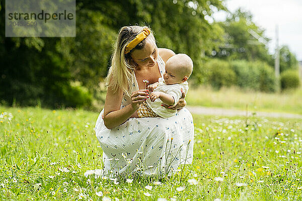 Mother giving flower to baby boy squatting in garden