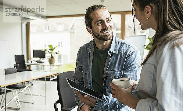 Smiling businessman holding tablet PC communicating with colleague at office