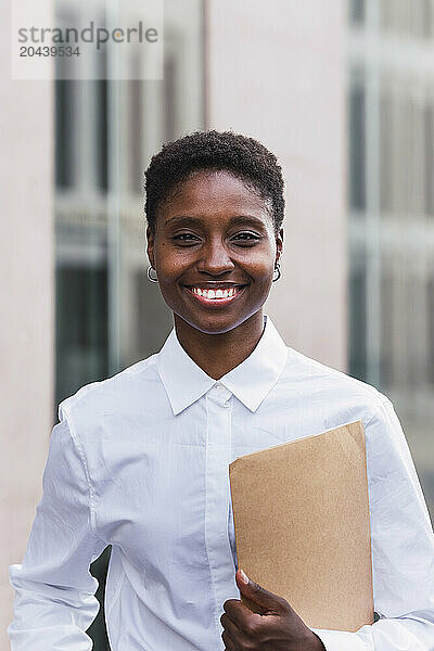 Smiling young businesswoman standing with document at office park