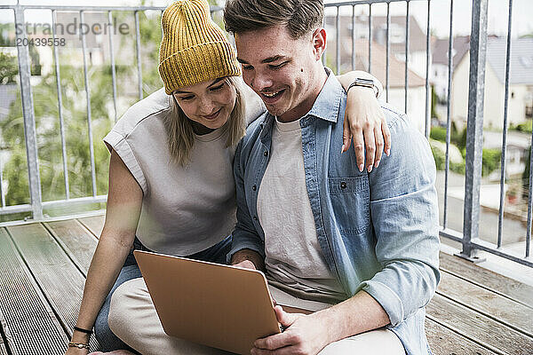 Smiling young couple using laptop on balcony