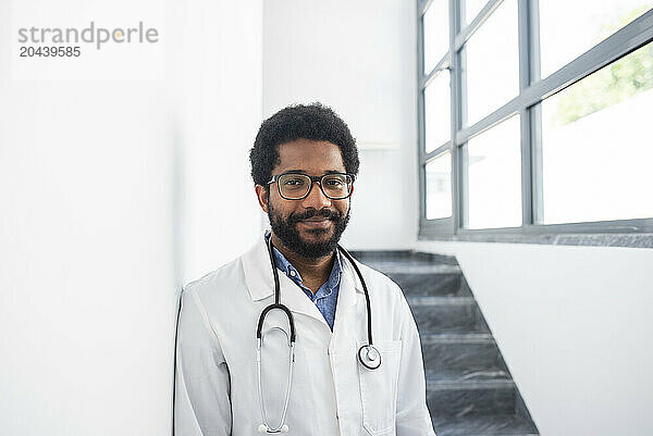 Smiling doctor wearing eyeglasses standing in hospital staircase