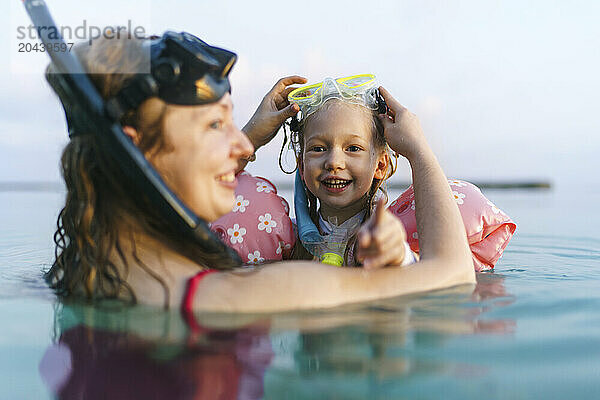 Smiling mother and daughter snorkeling together in sea at sunset