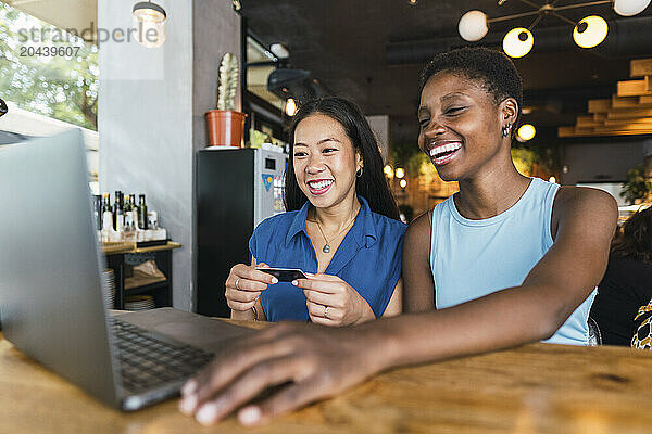 Happy women using laptop sitting with credit card at cafe