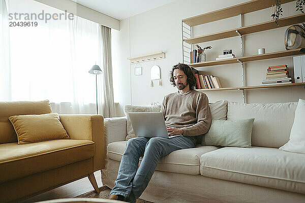 Businessman using laptop sitting on sofa working at home