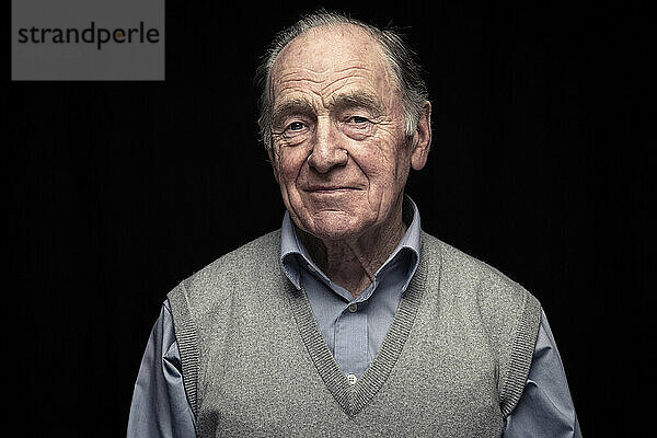 Wrinkled senior man standing against black background